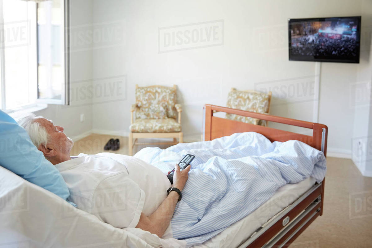 Senior man watching TV while reclining on bed in hospital ward Stock