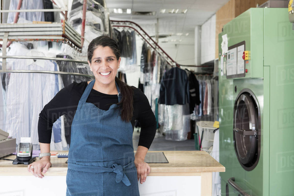 Portrait of smiling mature female dry cleaner standing at Laundromat ...