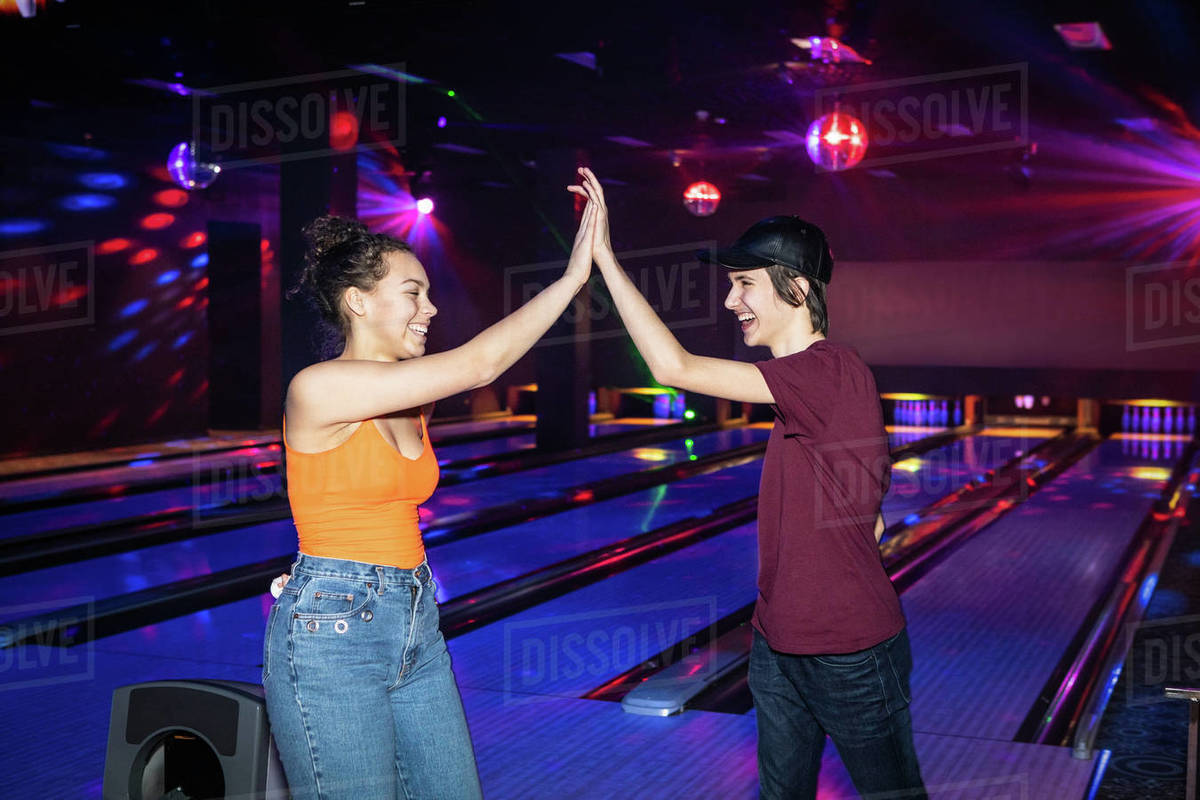 Cheerful friends giving highfive on illuminated parquet floor at