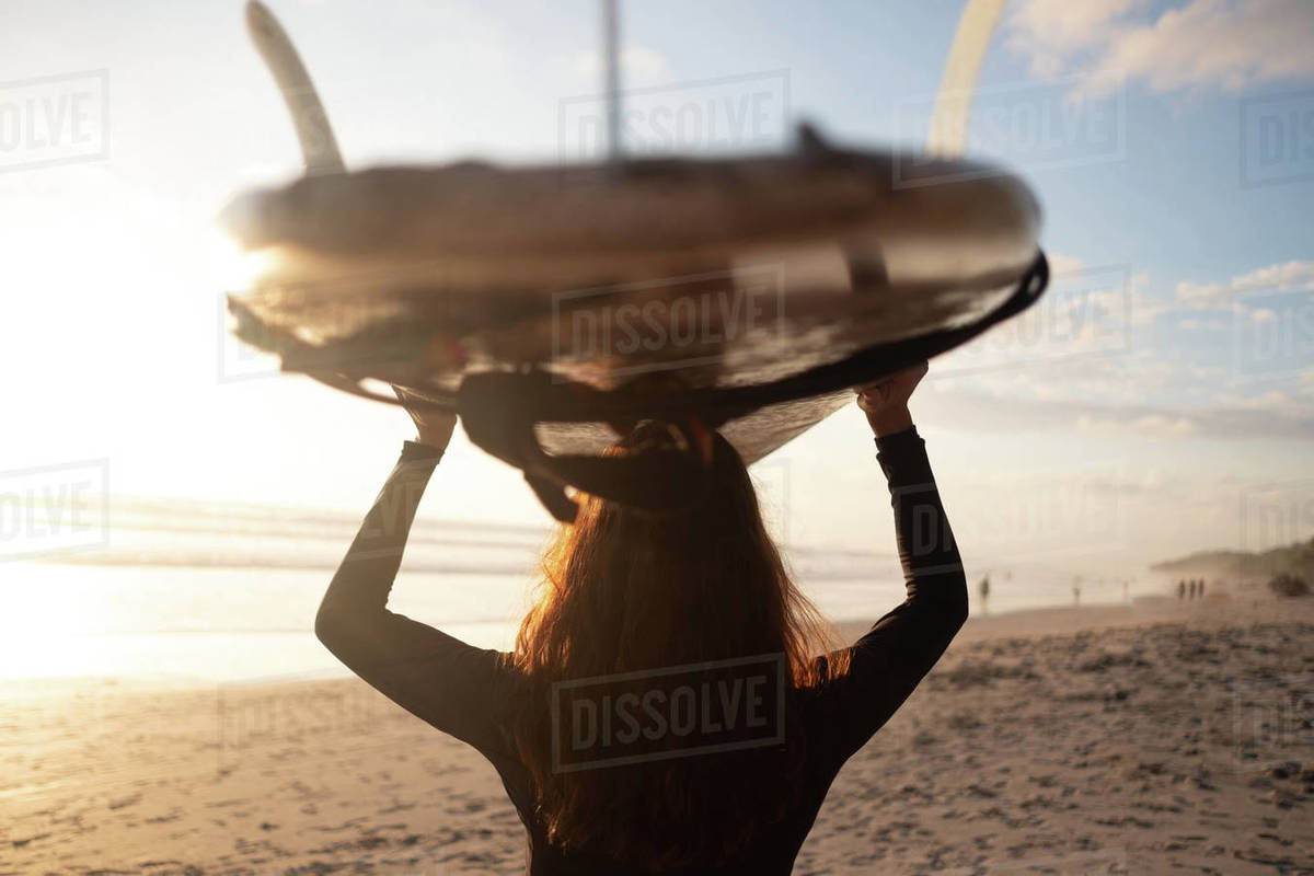 Rear view of mature woman carrying surfboard on head at beach Royalty-free stock photo