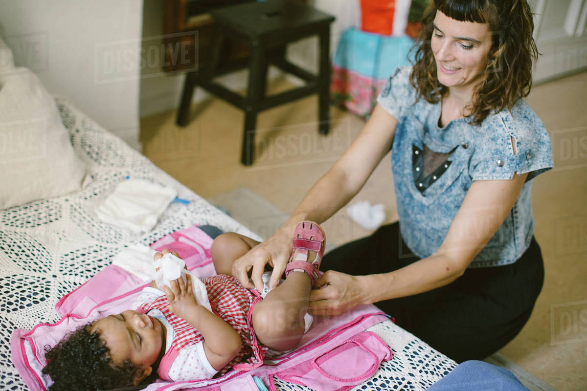 daghter diaper Mother adjusting diaper of daughter lying on baby carrier at home - Stock  Photo - Dissolve
