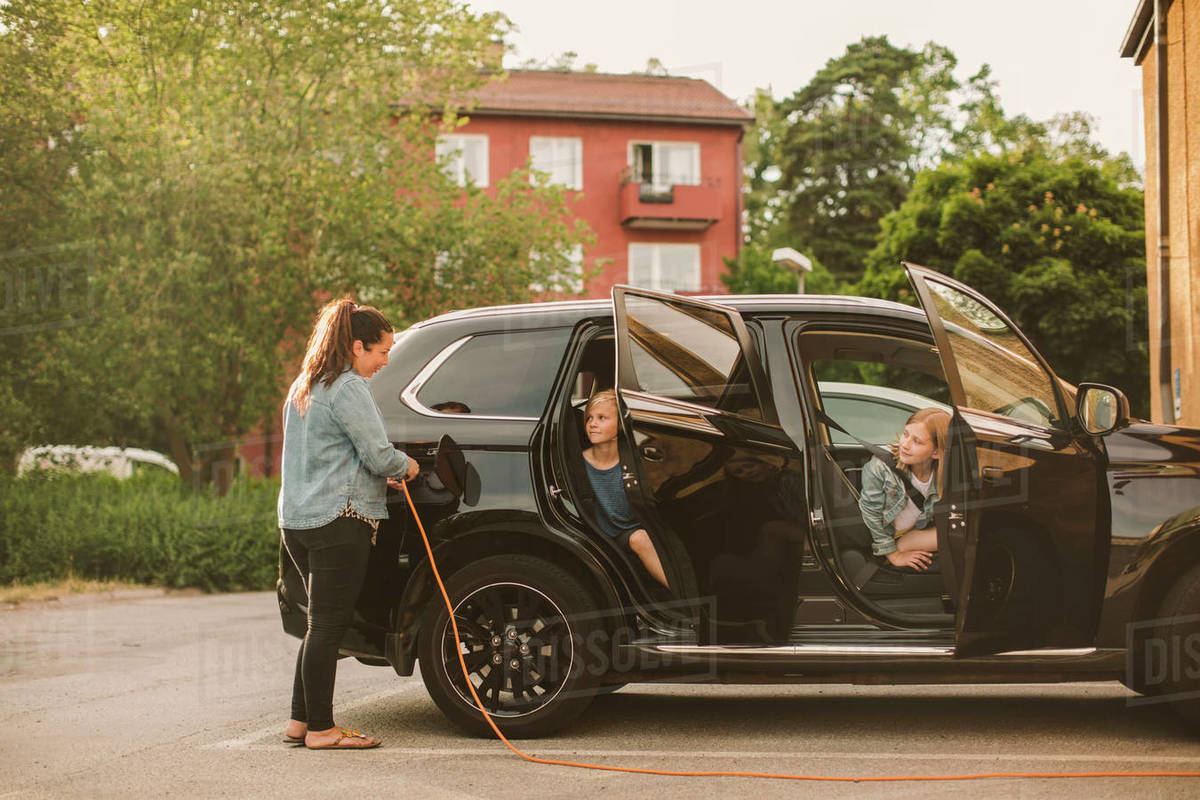 Girls looking at smiling mother charging electric car at station Royalty-free stock photo