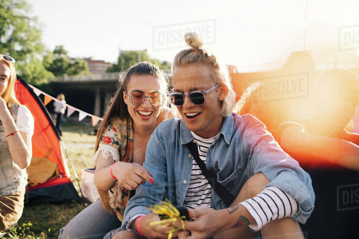 Smiling male and female friends looking at smart phone while sitting on lawn in sunny day Royalty-free stock photo