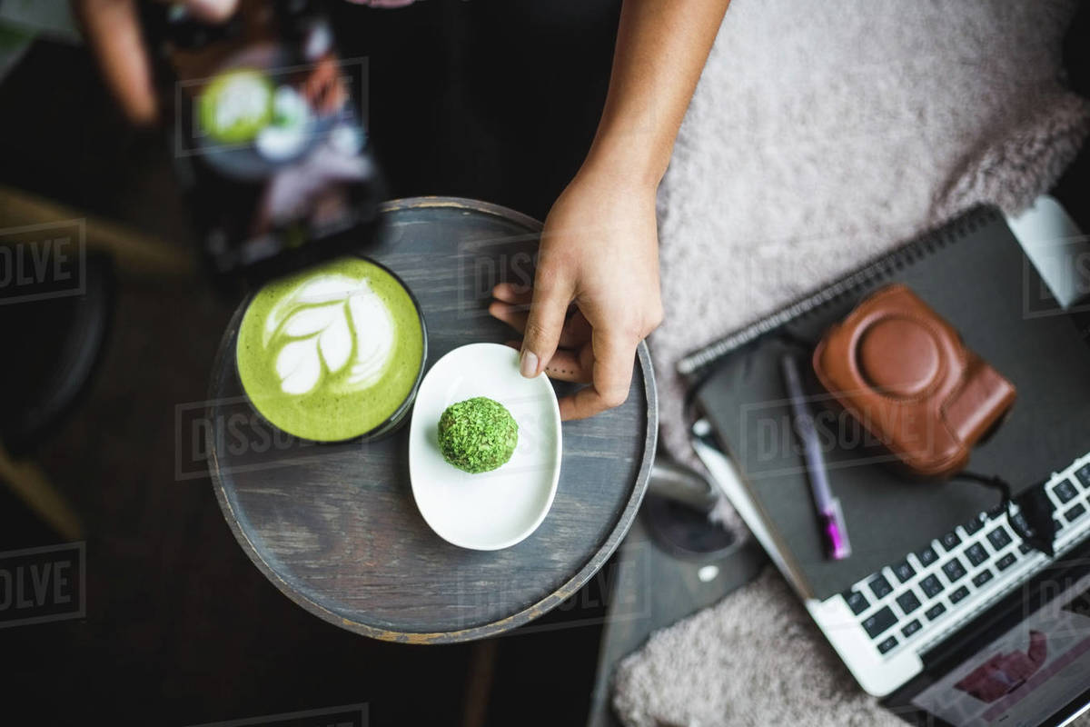 Directly above view of female blogger photographing matcha tea and snack through smart phone at creative office Royalty-free stock photo