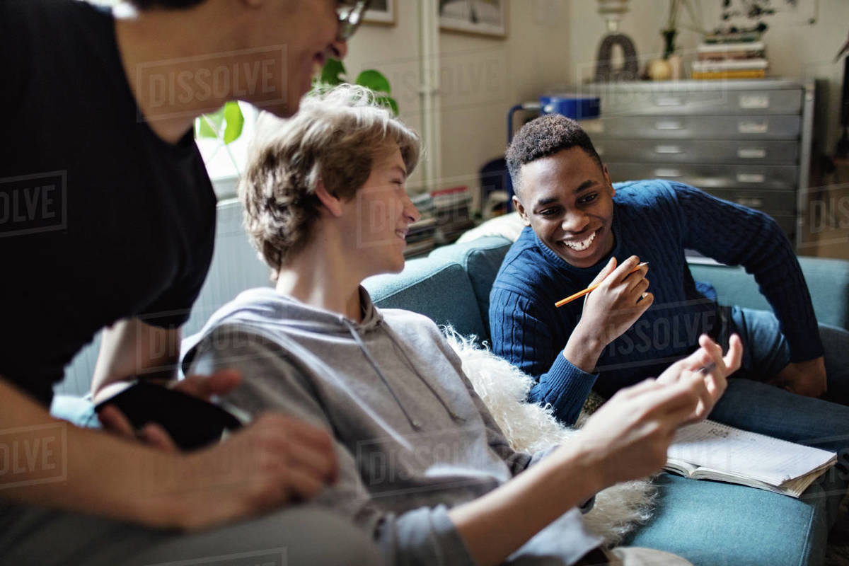 Smiling teenage boy showing mobile phone to friends on sofa while studying at home Royalty-free stock photo