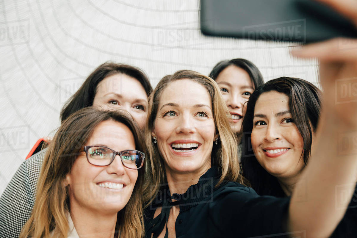 Smiling businesswoman taking selfie with female professionals at office during conference event Royalty-free stock photo