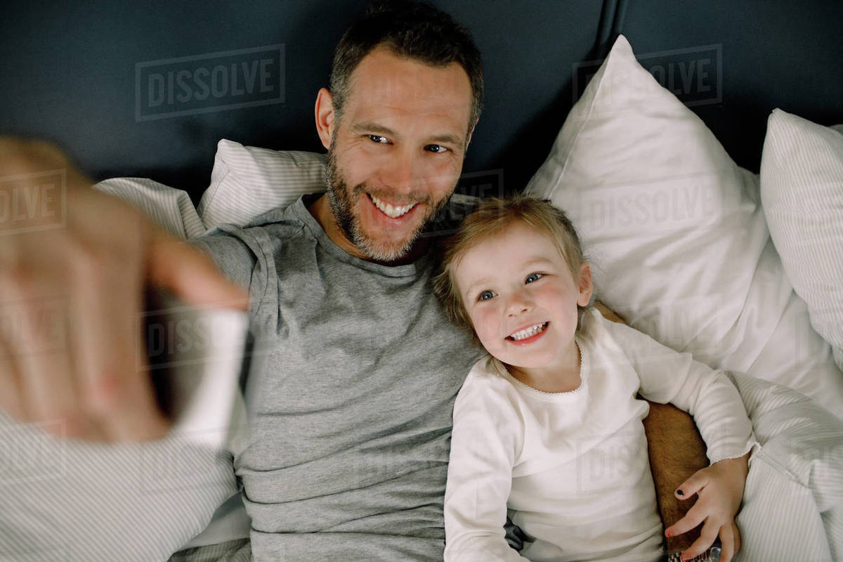 High angle view of happy father taking selfie with smiling daughter on bed in hotel Royalty-free stock photo