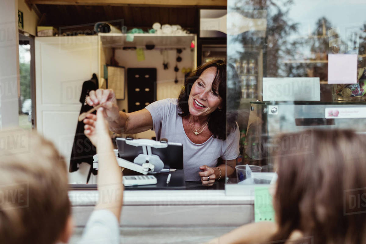 Smiling female owner giving spoon to customer standing by concession