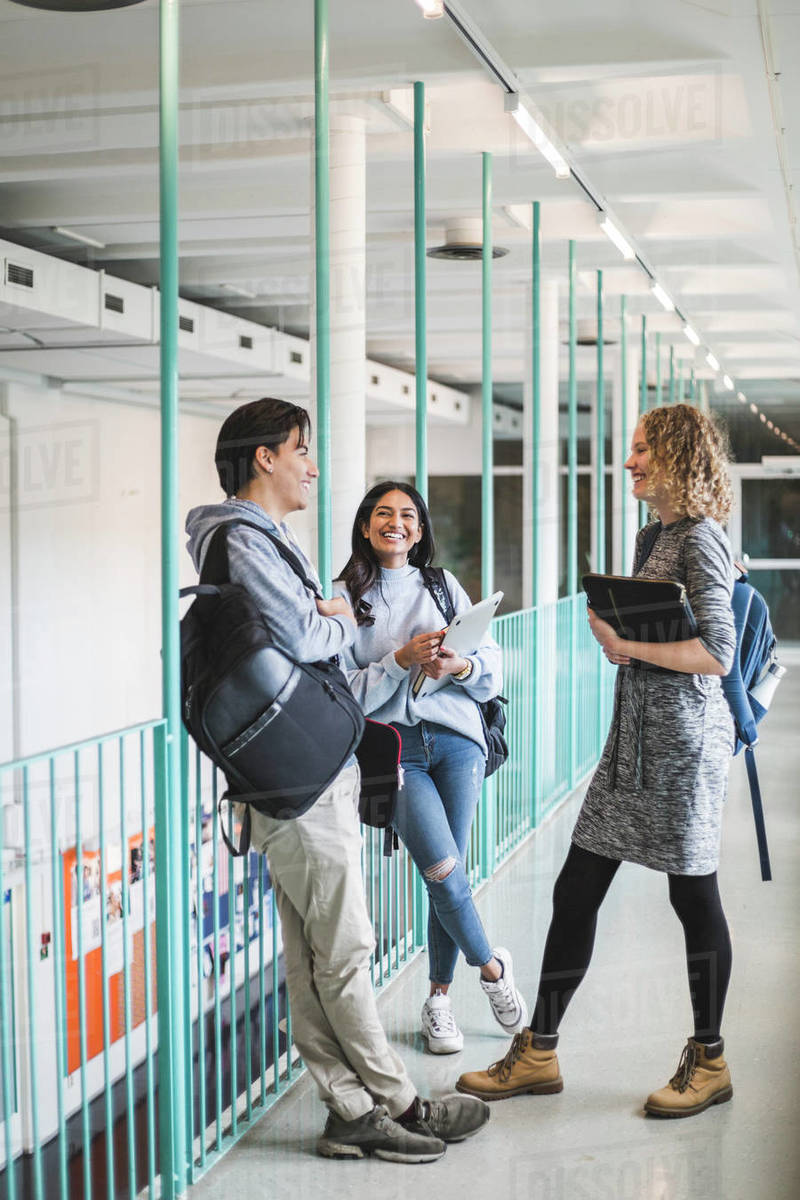 Male and female students talking while standing in corridor of ...