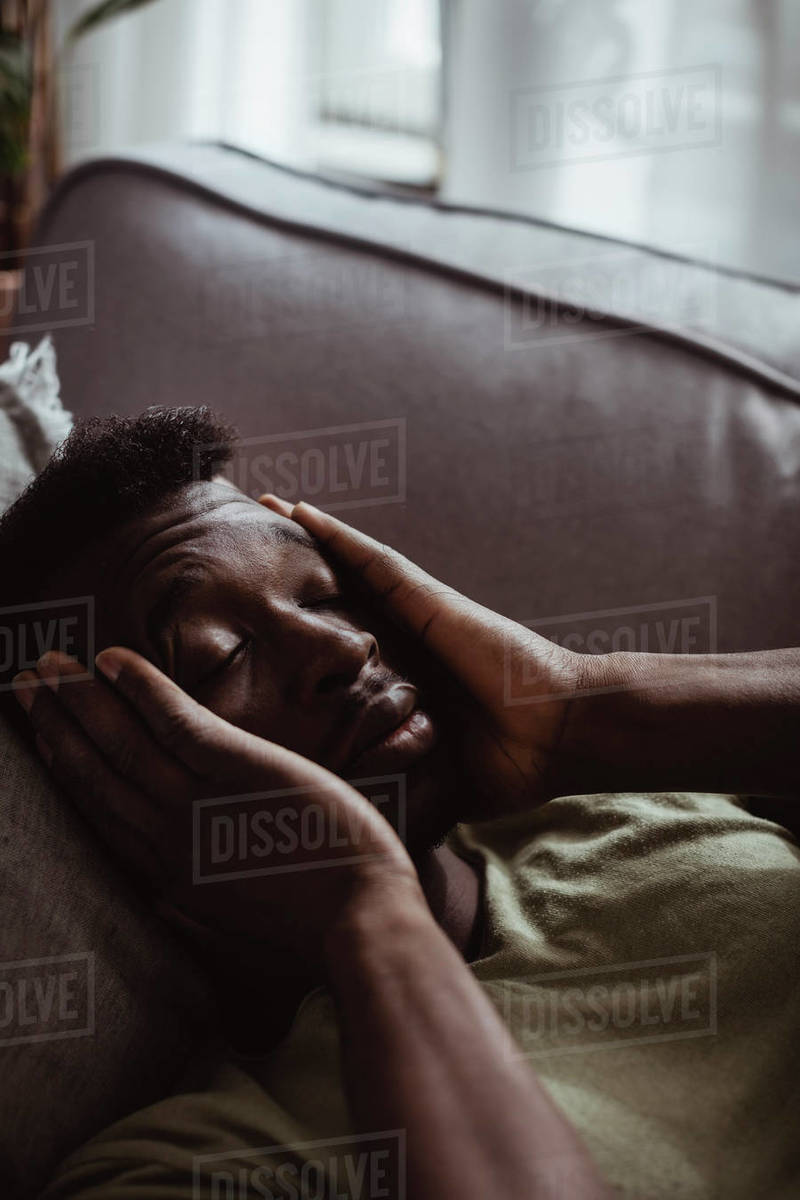 Closeup of man with headache lying on sofa in living room Stock