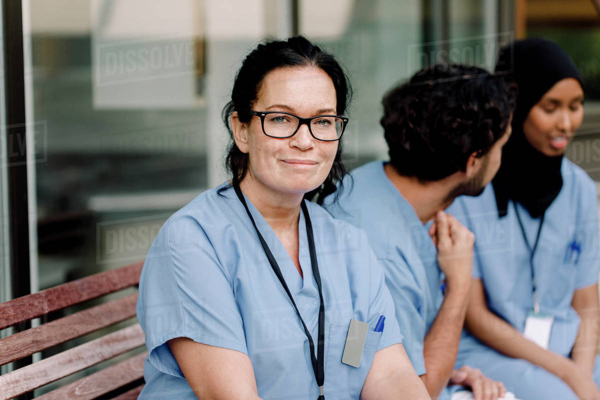 Portrait of smiling female nurse in eyeglasses sitting by colleagues on