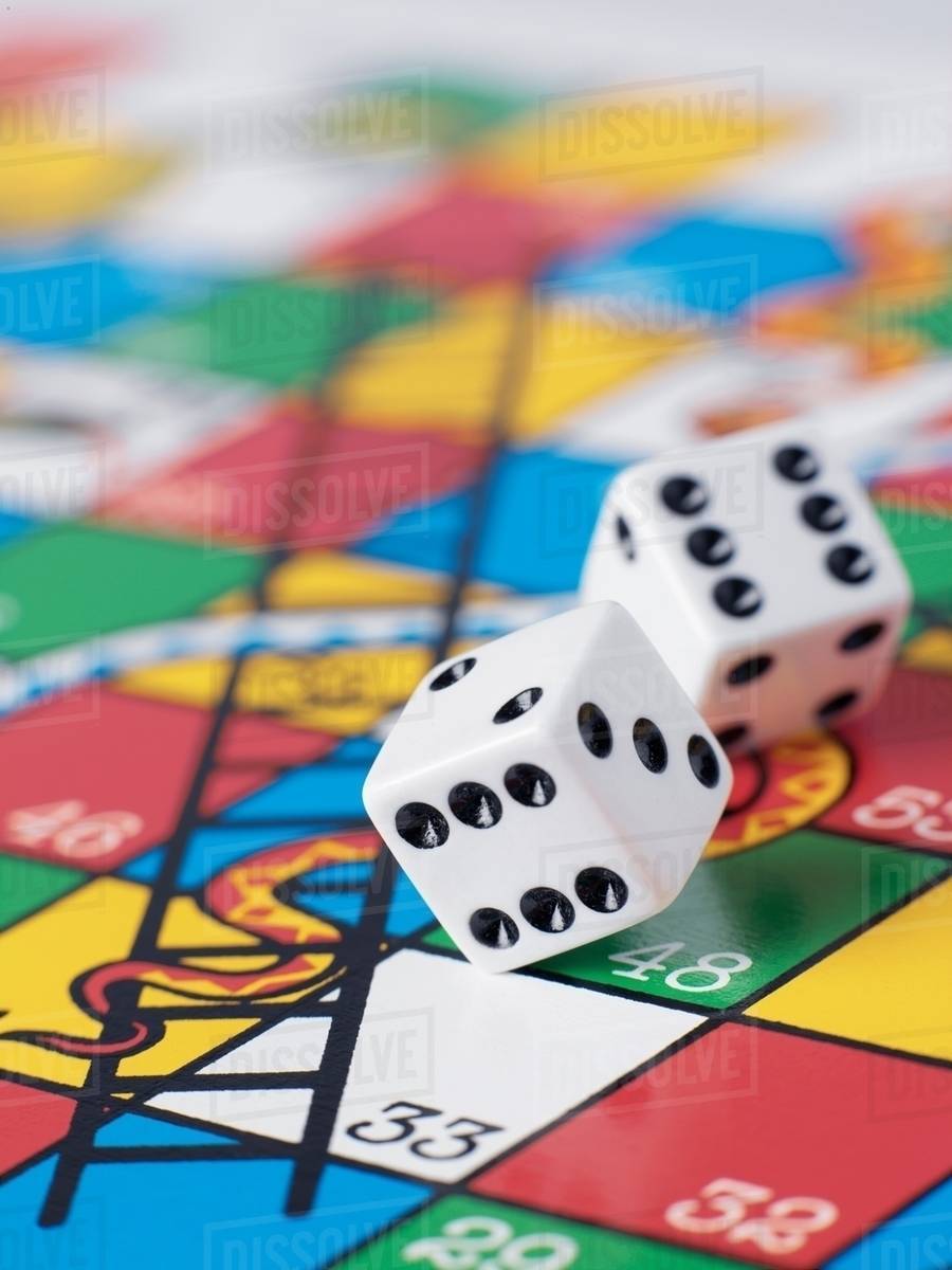Dice falling onto snakes and ladders board Stock Photo Dissolve