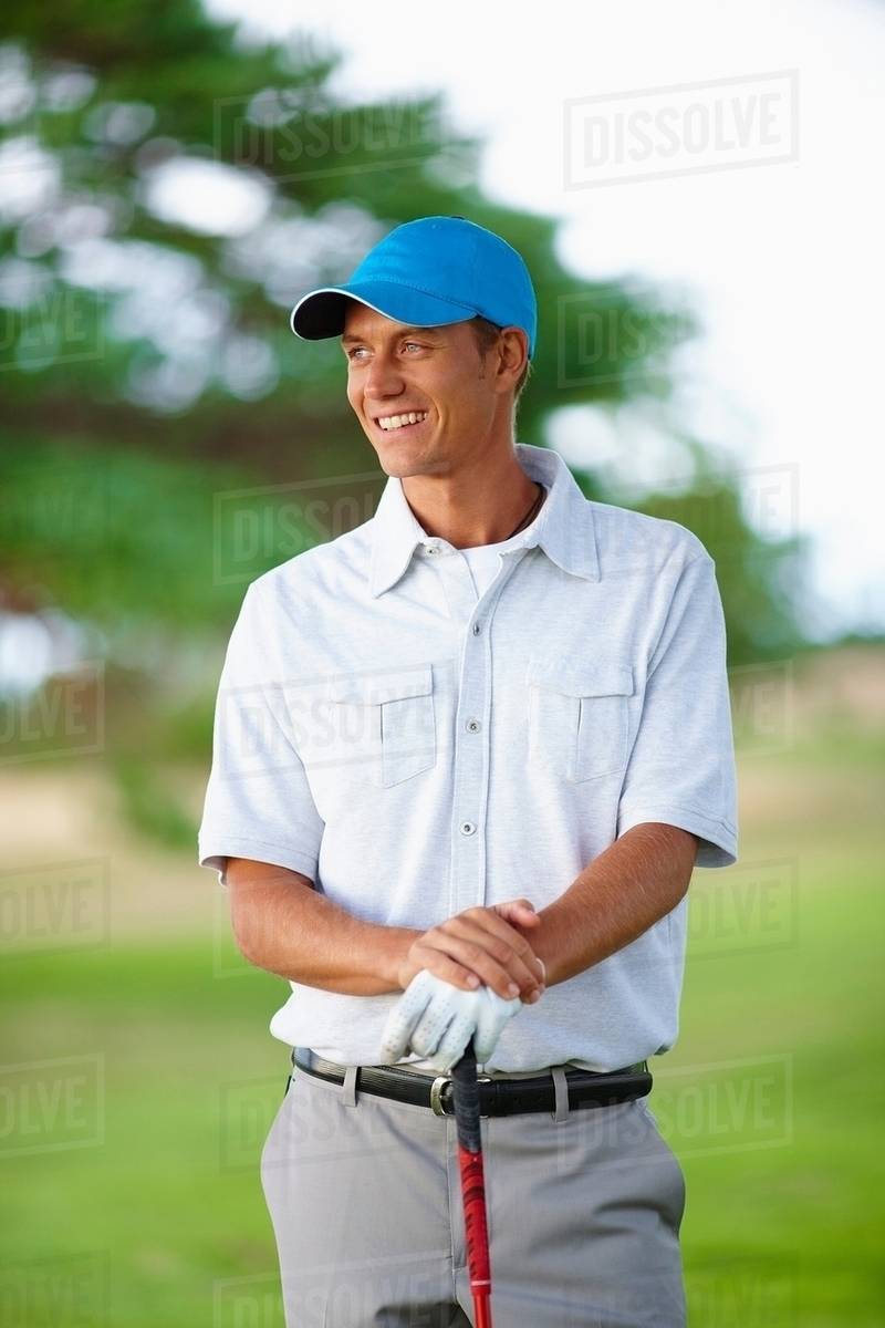 Golfer wearing golf glove and baseball cap holding golf club looking