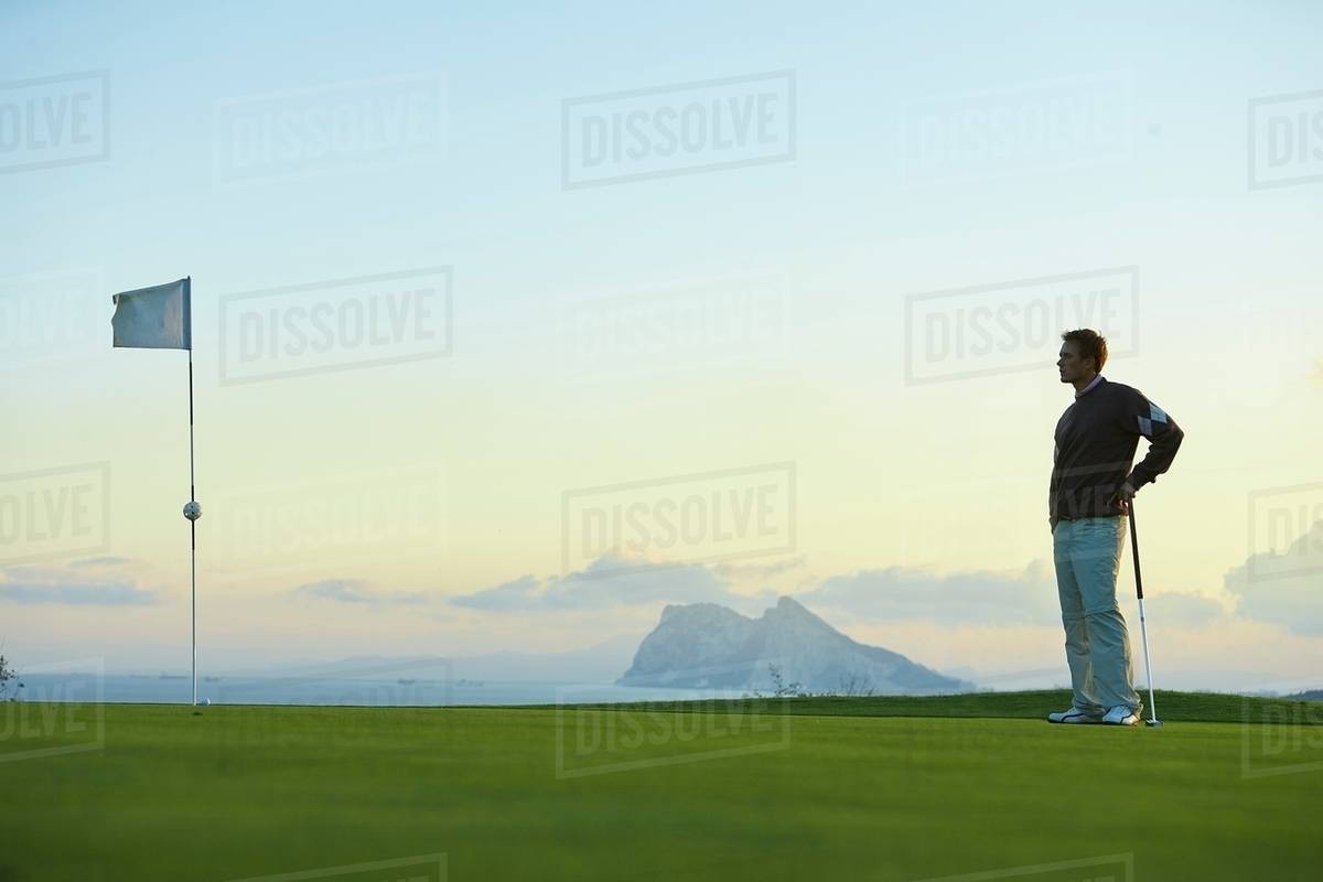 Golfer holding golf club standing near golf flag looking away Stock