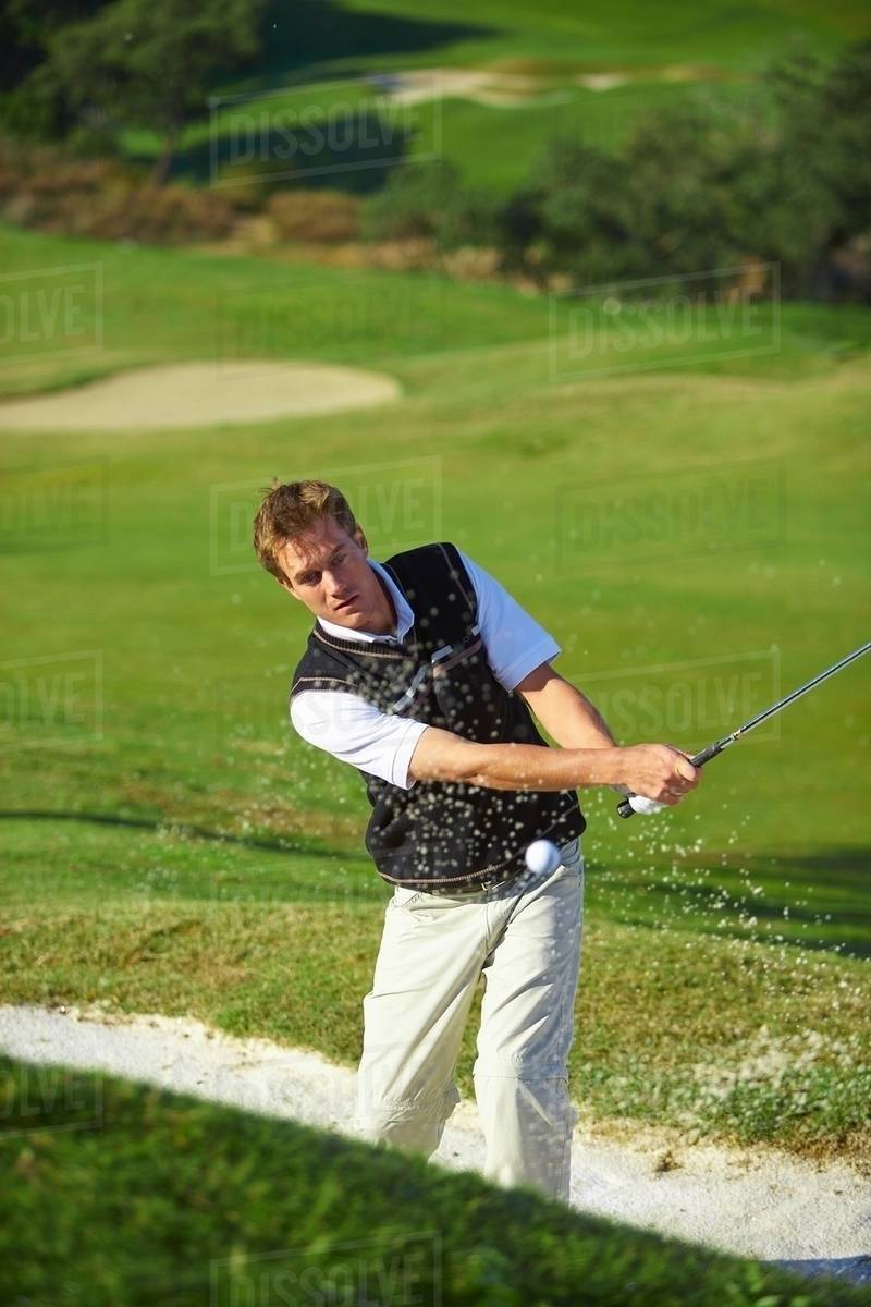 Golfer taking golf swing in sand trap, golf ball in mid air Stock