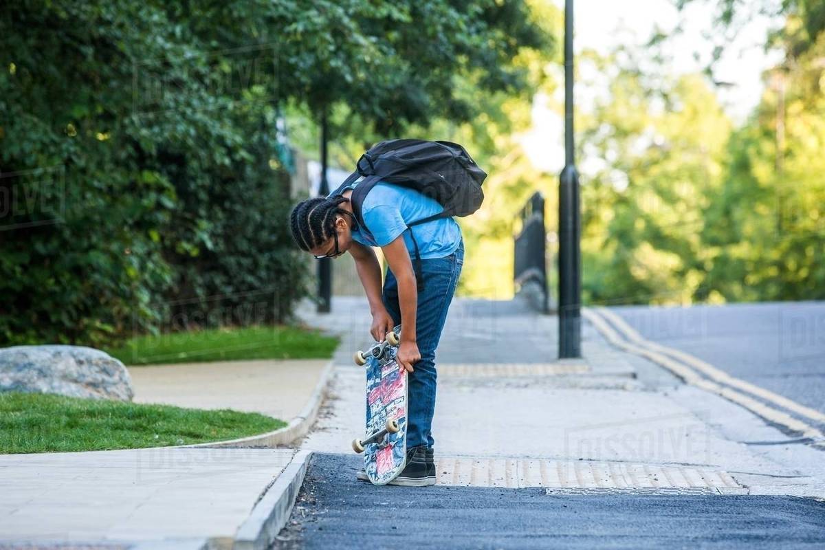 Boy checking his skateboard on sidewalk Stock Photo Dissolve