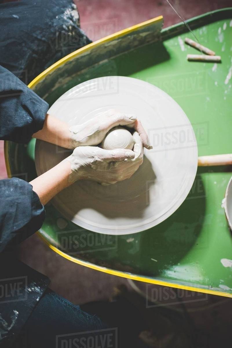 Overhead view of young womans hands shaping clay on pottery wheel