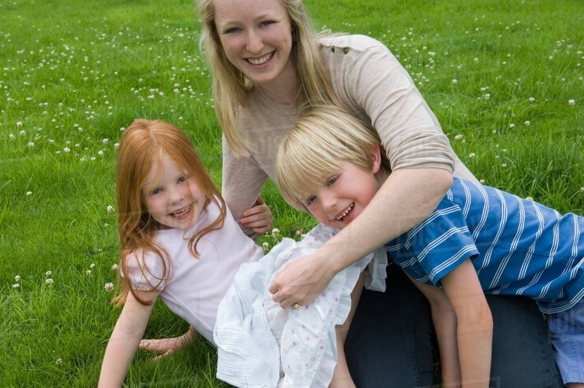 Mother and children playing in grass Stock Photo Dissolve