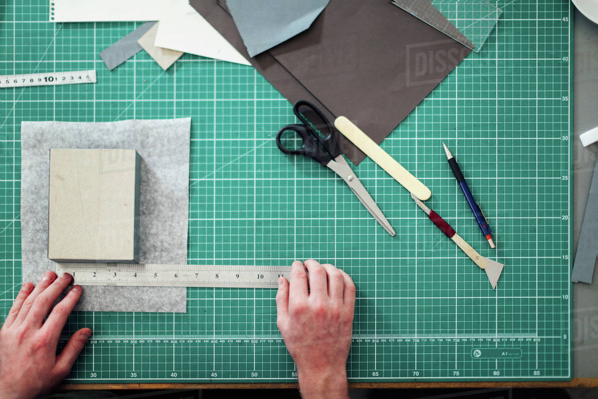 Overhead detail of hands, paper, cutting mat, ruler, scalpel and