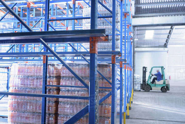 Worker packing water bottles in storage racking in spring water factory ...