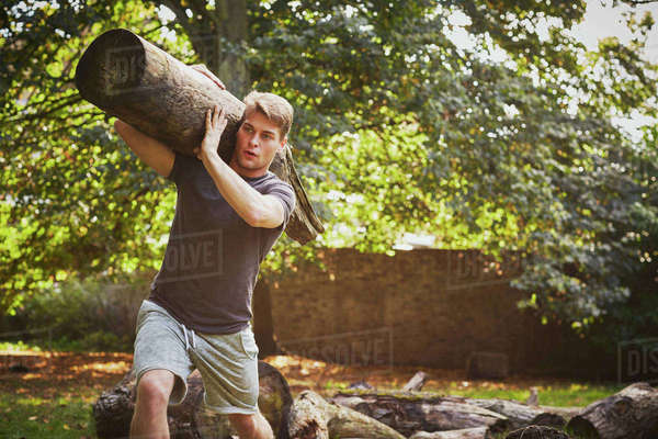 Young man training, lifting tree trunk on shoulder in park - Royalty ...