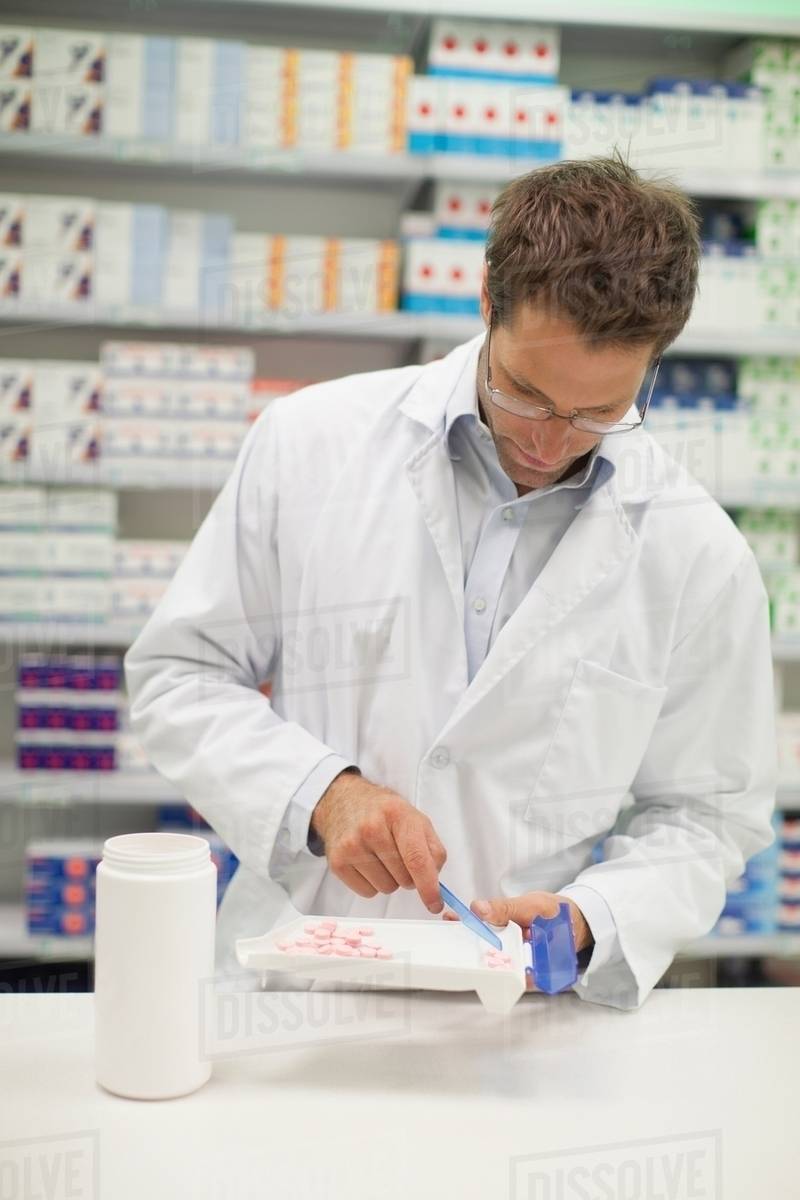 Pharmacist counting pills at counter Stock Photo Dissolve