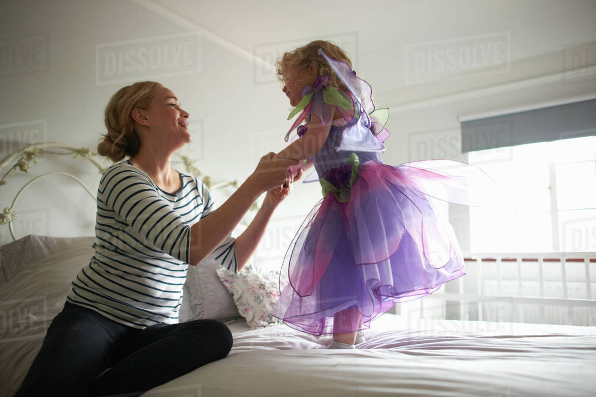 Young girl dressed in fairy costume, standing on bed, mother holding her hands Royalty-free stock photo