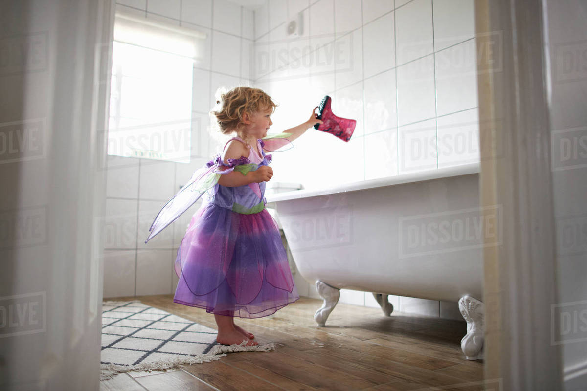 Young girl dressed in fairy costume, holding rubber boot over bathtub Royalty-free stock photo