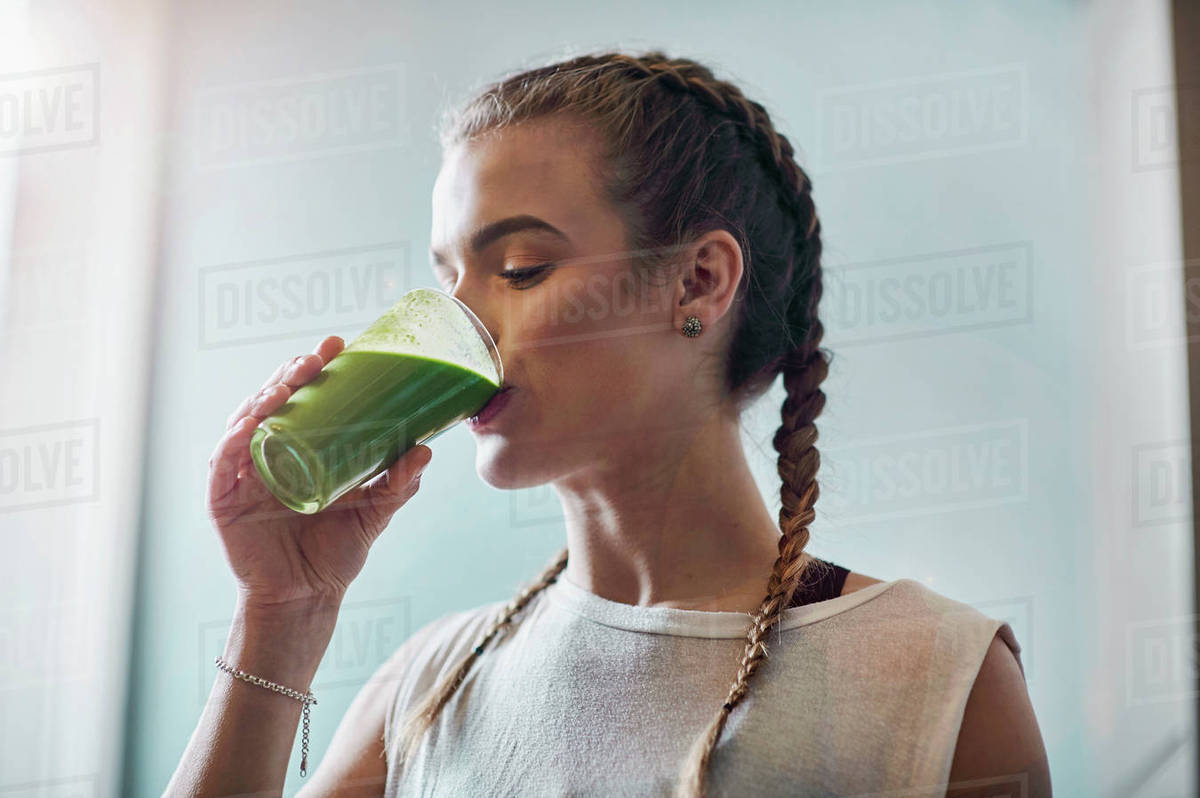Young woman drinking vegetable smoothie in kitchen Stock Photo Dissolve