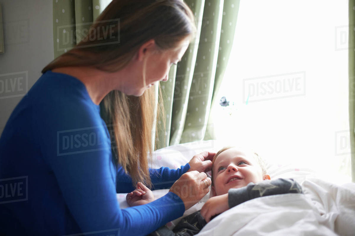 Boy lying in bed gazing at mother Stock Photo Dissolve