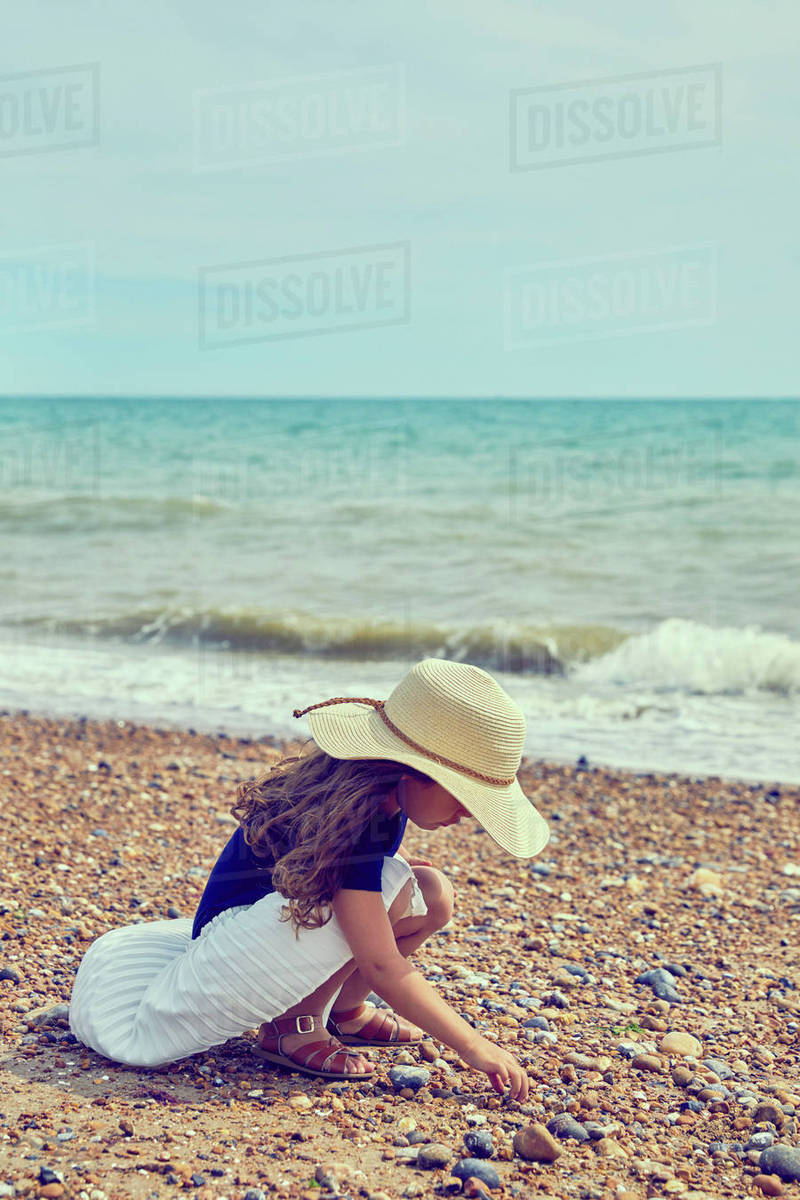 Young girl crouching on beach, collecting shells Stock Photo Dissolve