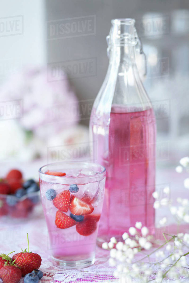 Glass of berry cordial with fresh fruit, bottle of cordial beside glass