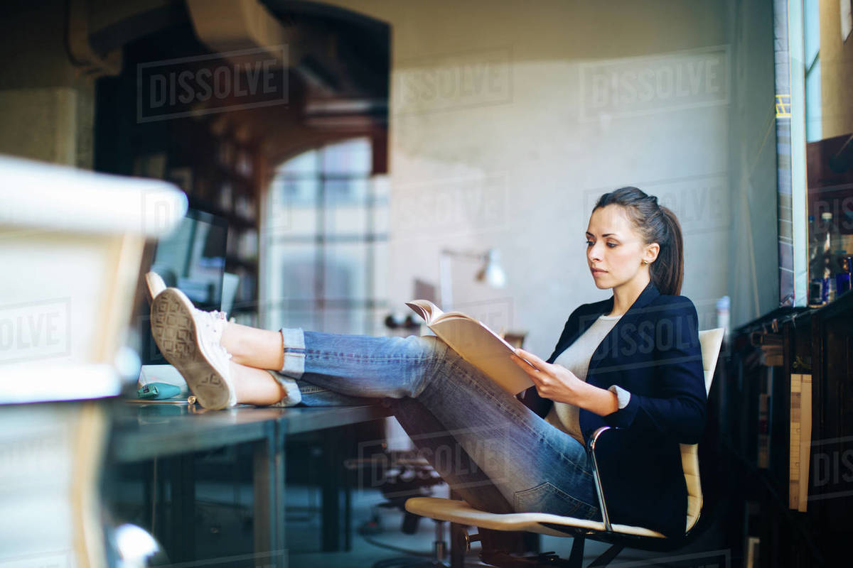 Businesswoman Sitting At Desk Feet Up On Looking Documents Stock Photo
