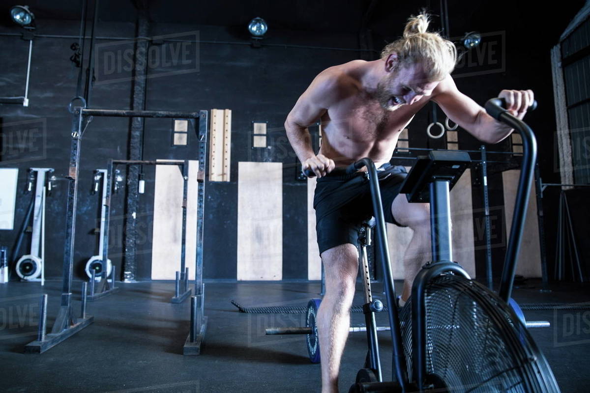 Man exercising in gymnasium, using air resistance exercise bike Stock