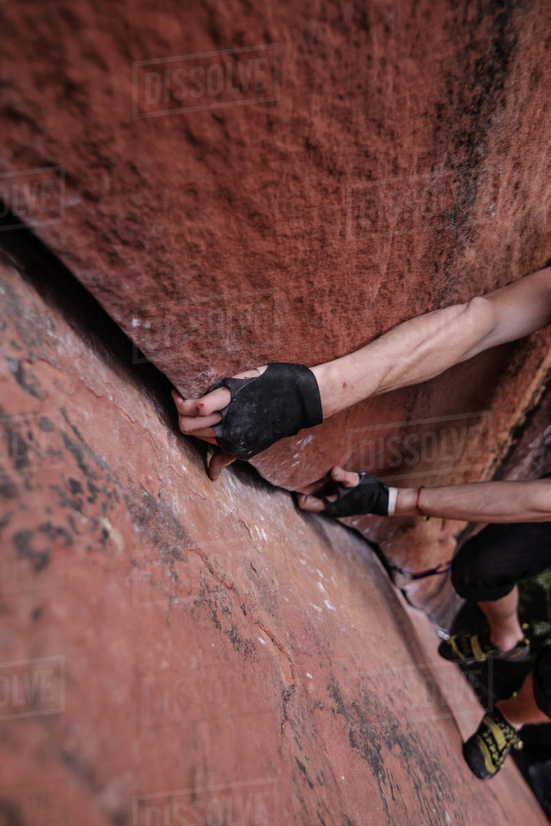 Rock climber climbing sandstone rock, hands gripping rock, elevated