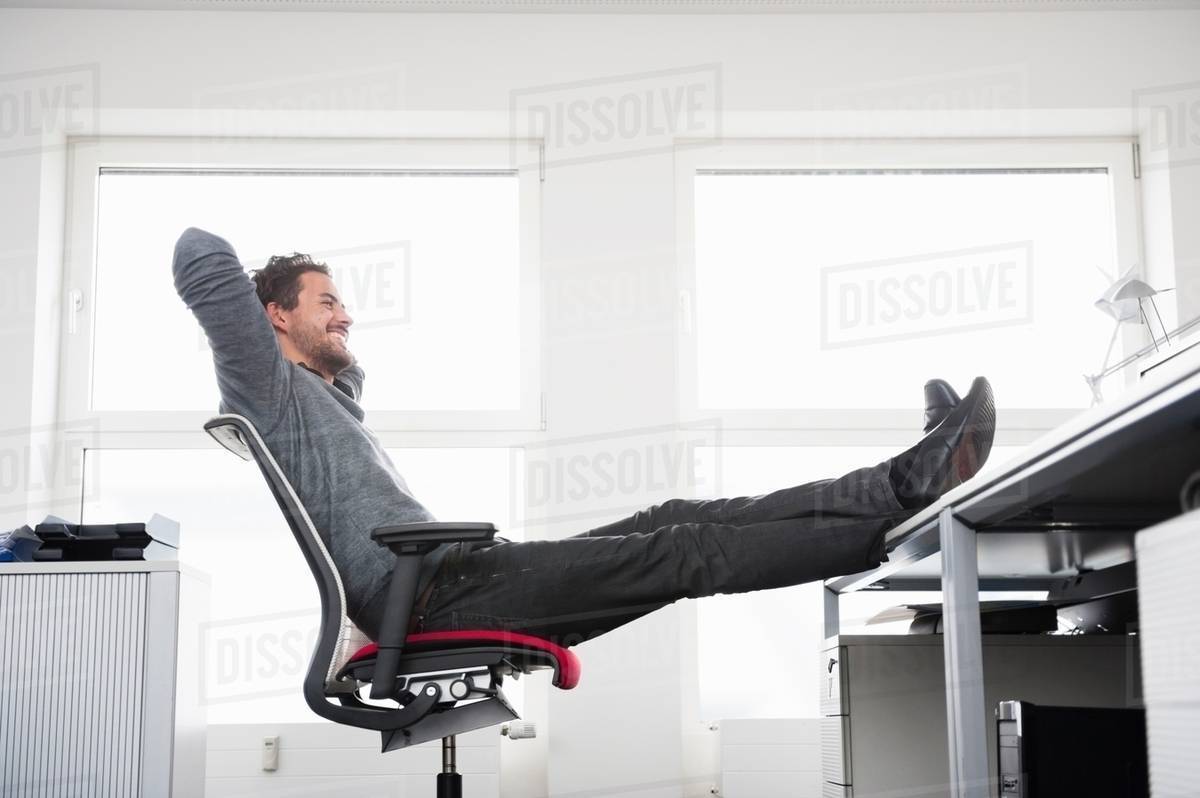 Man Sitting On Office Chair With Feet Up Desk Stock Photo