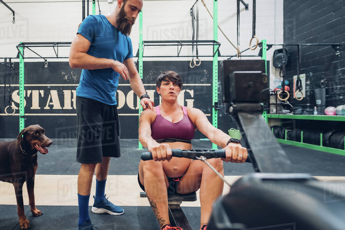 Trainer guiding pregnant woman on rowing machine in gym Stock Photo