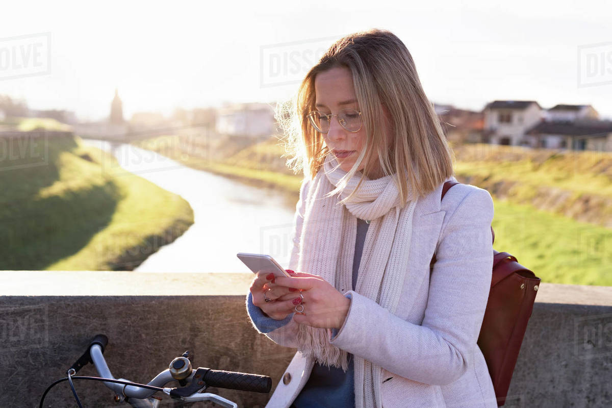 Female higher education student on river bridge looking at smartphone, Florence, Italy Royalty-free stock photo