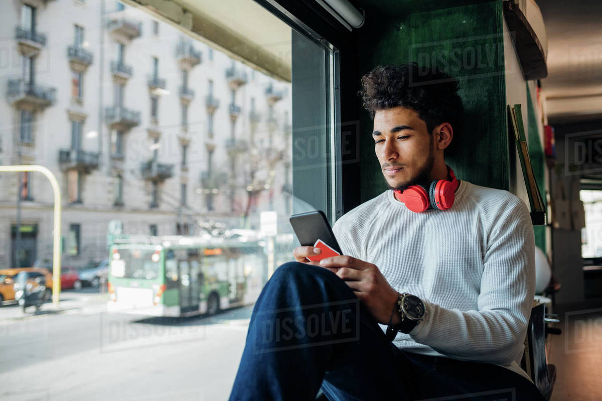 Young man looking at smartphone in cafe window seat Royalty-free stock photo