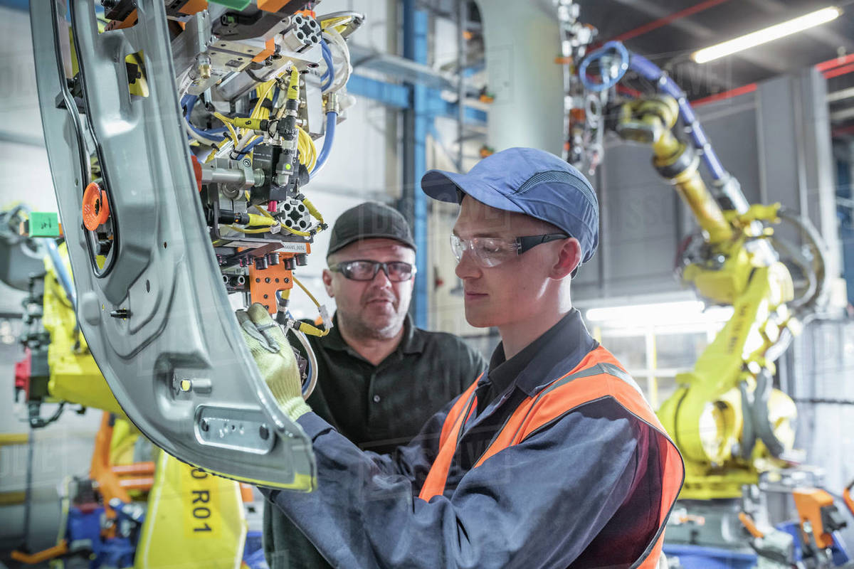 Apprentice engineer with mentor and robots in car factory Royalty-free stock photo