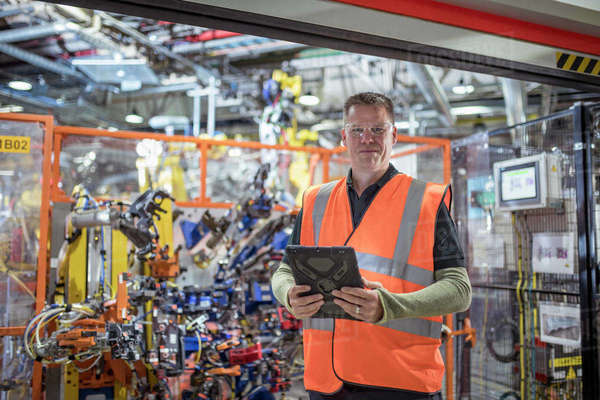 Portrait of computer programmer with robots in car factory - Stock ...