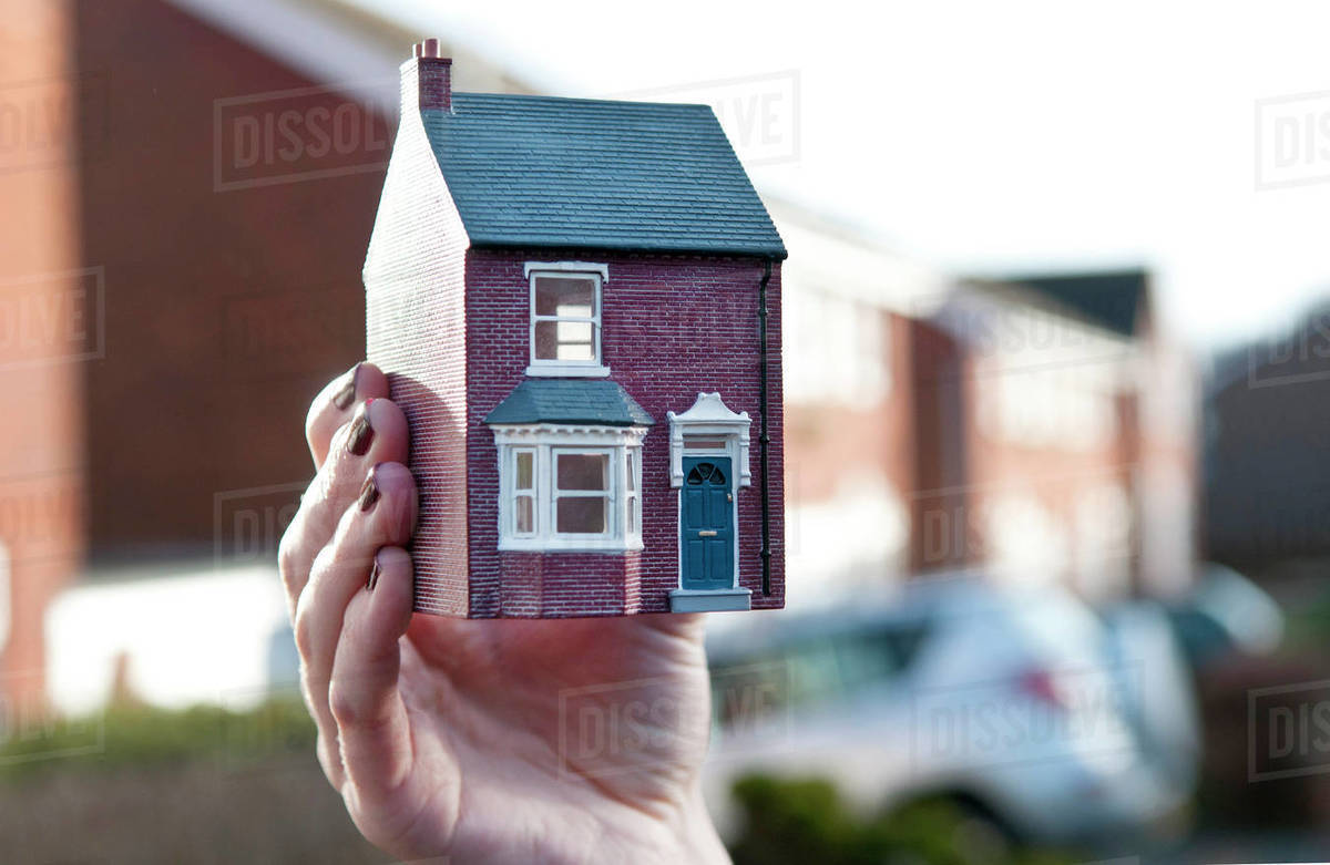 Teenage girl holding man made model of house in front of housing estate, shallow focus, close up of hand Royalty-free stock photo