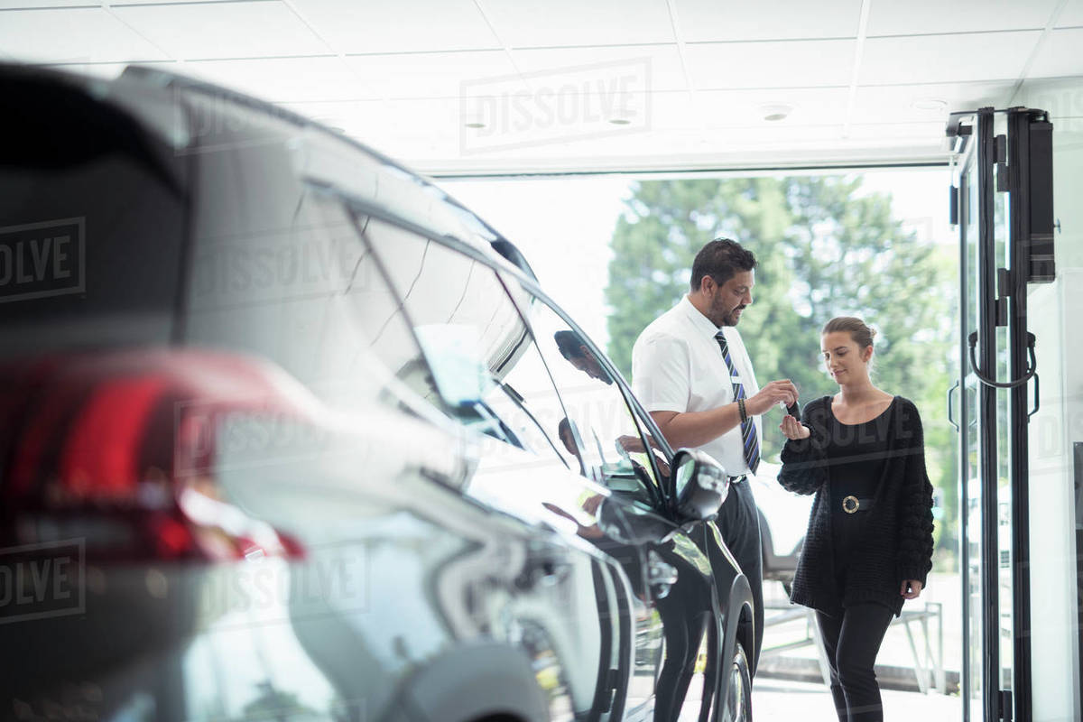 Salesman handing over new car keys to customer in car dealership Royalty-free stock photo