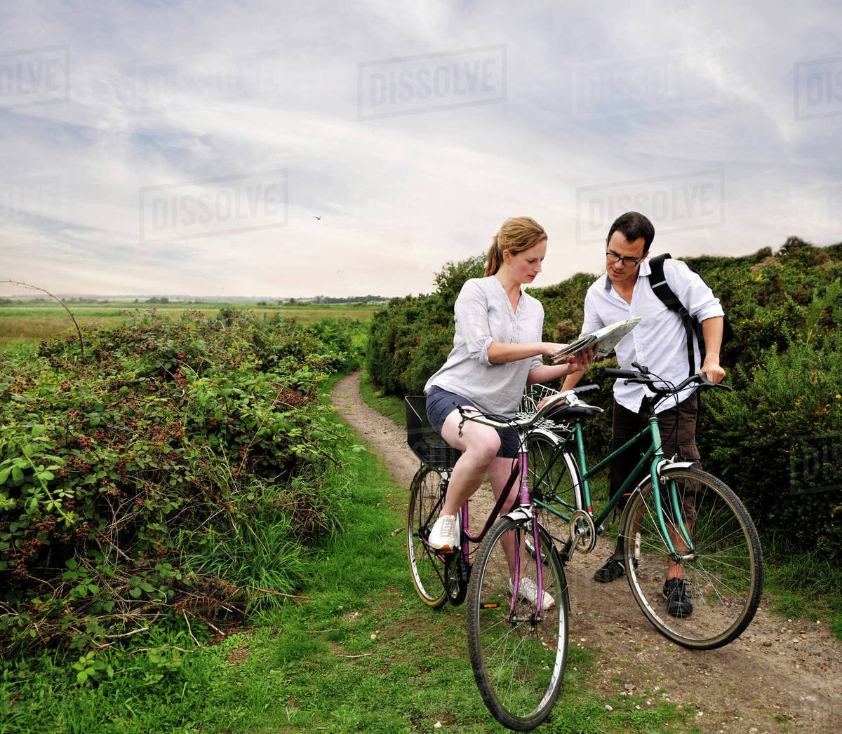 Mid adult cycling couple on rural dirt track looking at map, Southwold, Suffolk, UK Royalty-free stock photo