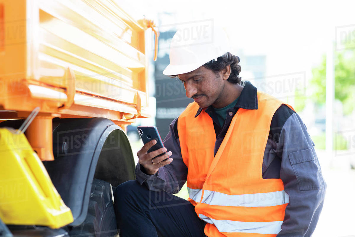 Male engineer standing next to yellow truck looking at smartphone Royalty-free stock photo