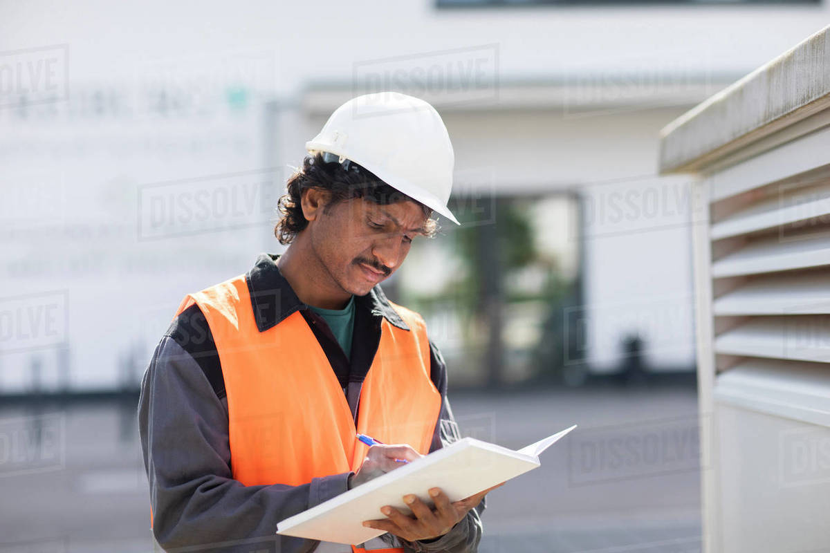 Male engineer outside industrial building writing in notebook Royalty-free stock photo