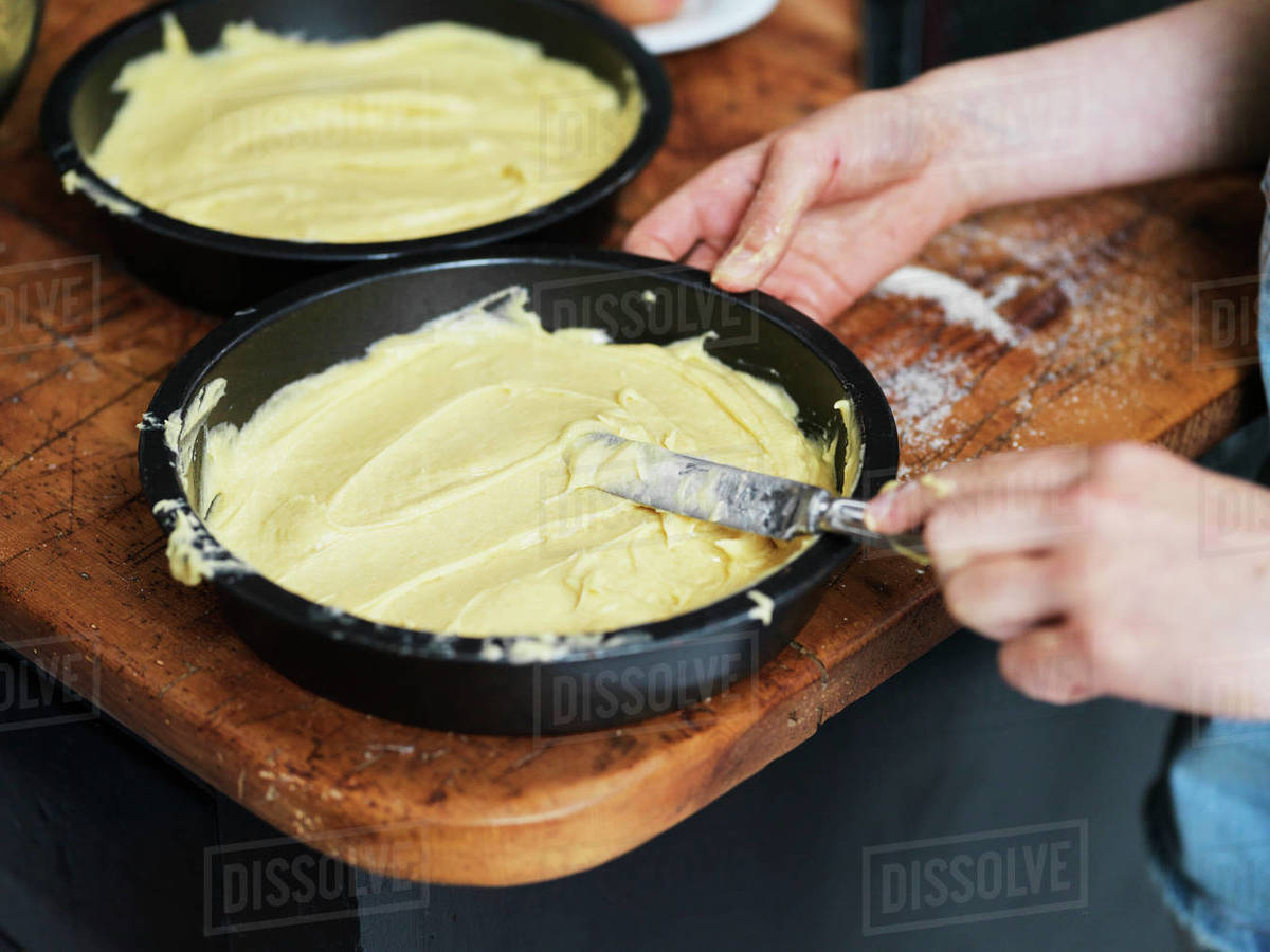 Girl baking a cake, smoothing cake mixture in cake tin at kitchen table, cropped close up of hands Royalty-free stock photo