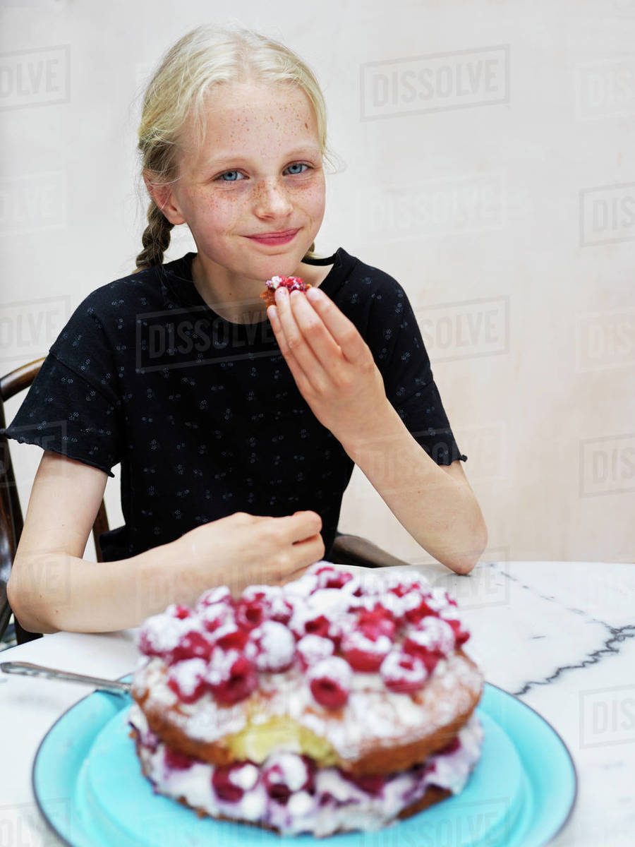 Girl eating her homemade cake with fresh raspberries at kitchen table, portrait Royalty-free stock photo