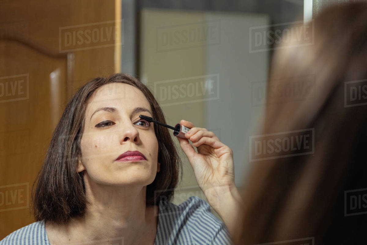 Woman standing in front of mirror, applying makeup Stock Photo Dissolve