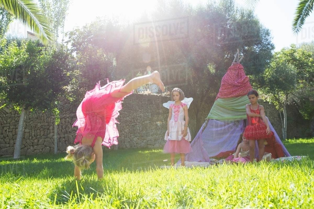 Girls watching friend in fairy costume doing handstand in garden Royalty-free stock photo